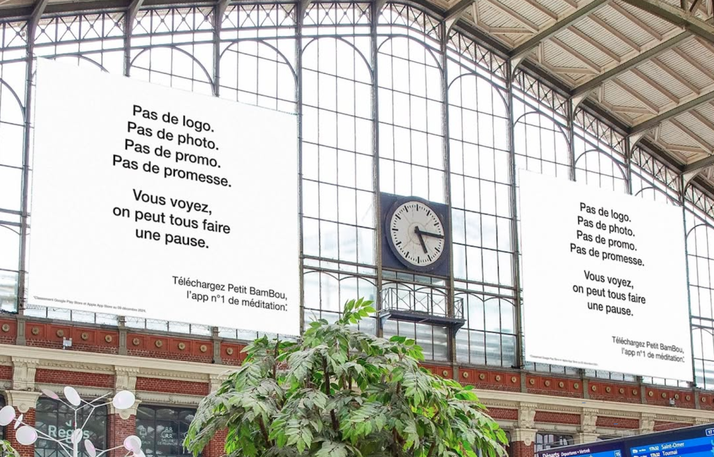 Affiche minimaliste Petit Bambou – Campagne “Invisible” Exemple de Quiet Marketing - Affiche minimaliste de la campagne publicitaire “invisible” de l’application de méditation Petit Bambou, placée dans une gare, invitant les passants à faire une pause. Source : Dans Ta Pub.