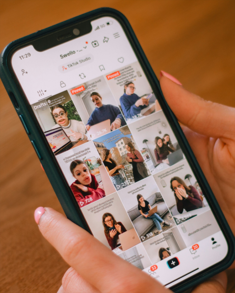 Main tenant un smartphone affichant la page TikTok Studio du compte Swello avec une grille de vidéos